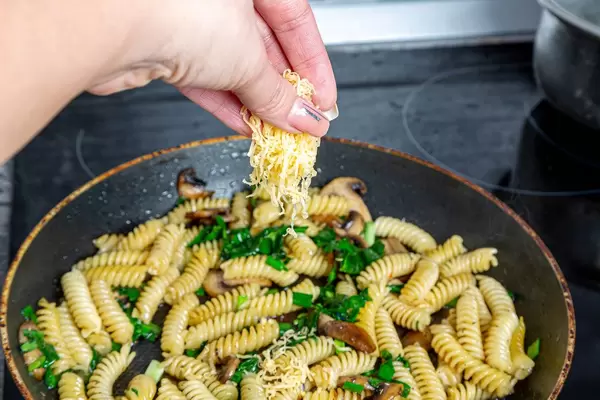 Female hand adds cheese to a pasta pan