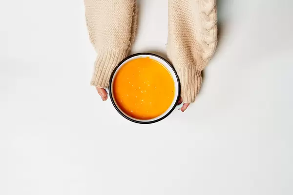 Female hand holding a bowl with pumpkin cream soup