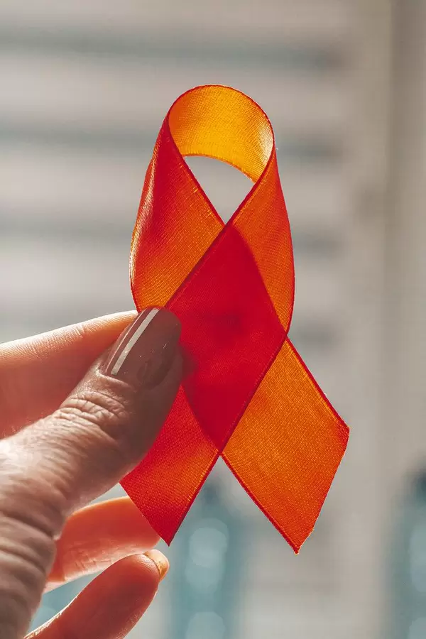 Female hand holding red ribbon on city background