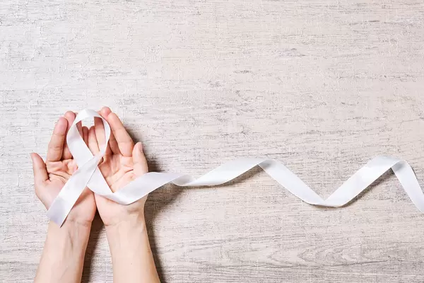 Female hand holding white ribbon awareness on wooden background with copy space