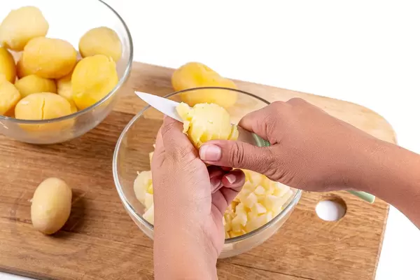Female hands cutting boiled potatoes into cubes with a ceramic knife