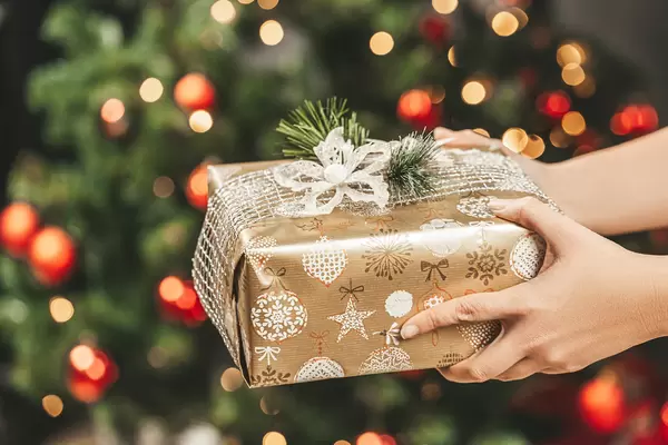 Female hands hold a gift on a blurred background of a decorated christmas tree