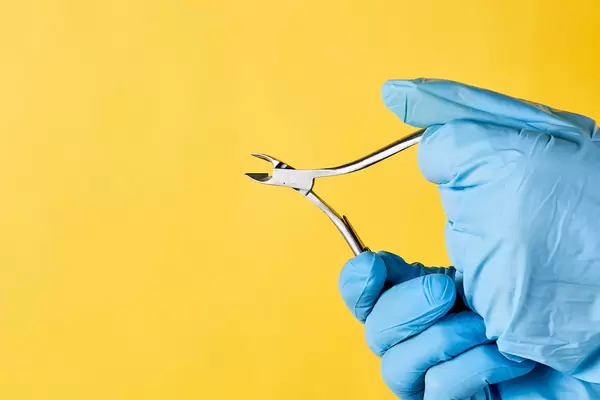 Female hands hold cuticle nipper over yellow background