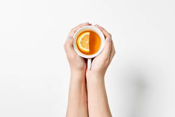 Female hands holding a cup of tea with lemon on white background