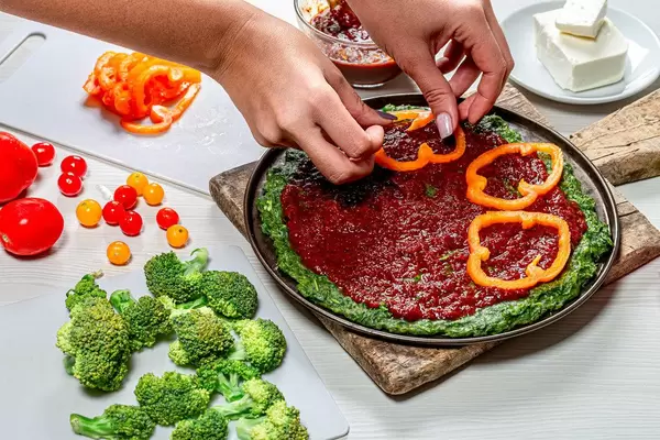 Female hands impose pieces of bell pepper on pizza. The concept of cooking healthy food (Flip 2019)