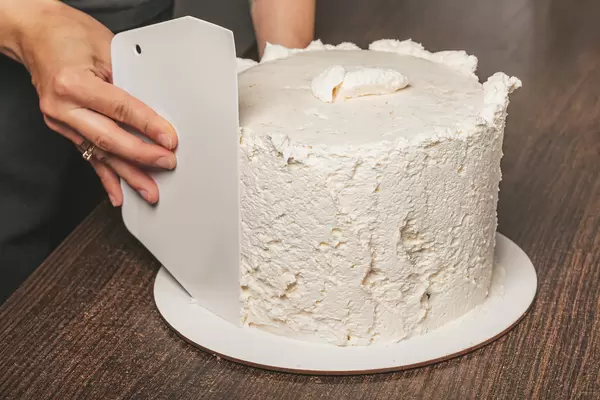 Female hands line creamy coating on cake, homemade baking