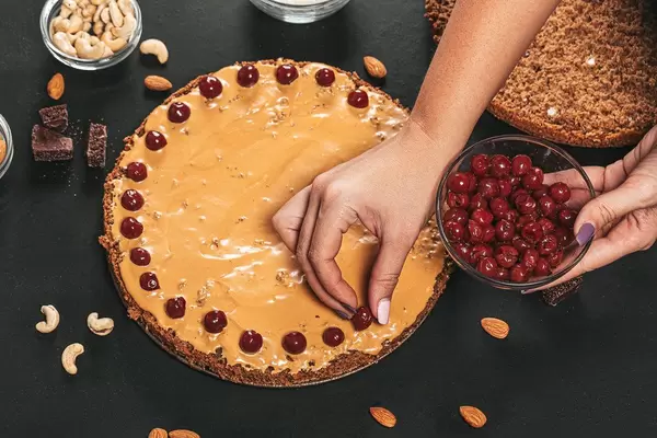 Female hands put alcoholized pitted cherry on cake cream