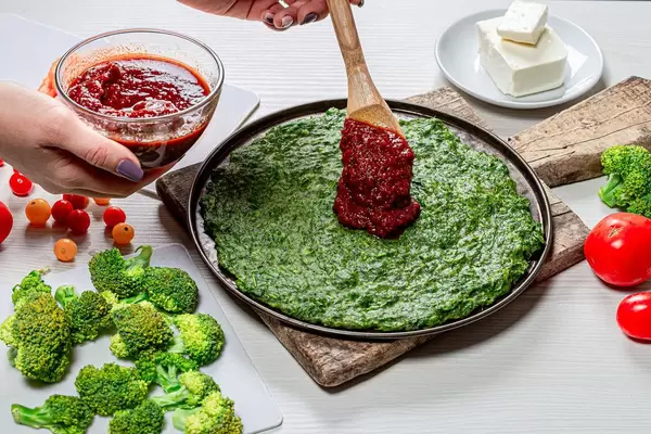 Female hands with a wooden spoon puts sauce on the pizza base (Flip 2019)