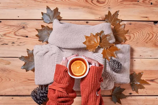 Female holds a cup of hot lemon tea over fall leaves