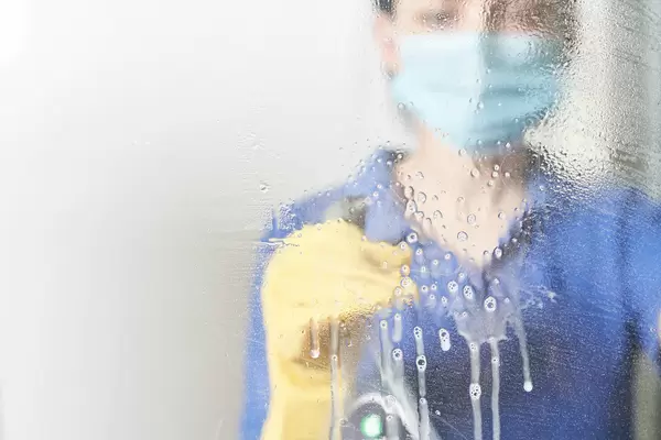 Female in face mask pouring cleaning spray on the glass surface