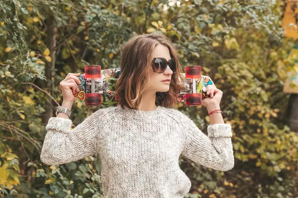 Female skateboarder holding a skateboard behind her head