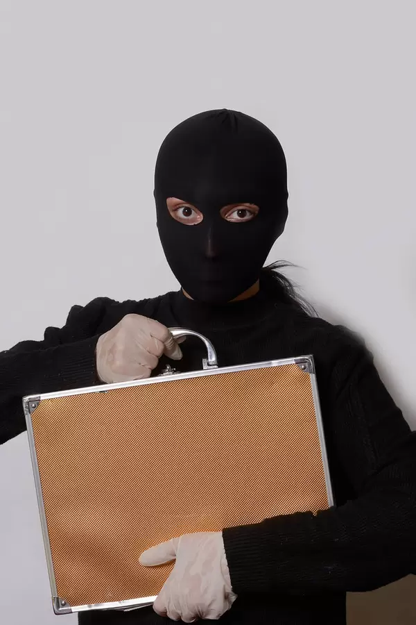 Female thief with balaclava on head holding a suitcase with cash and gems