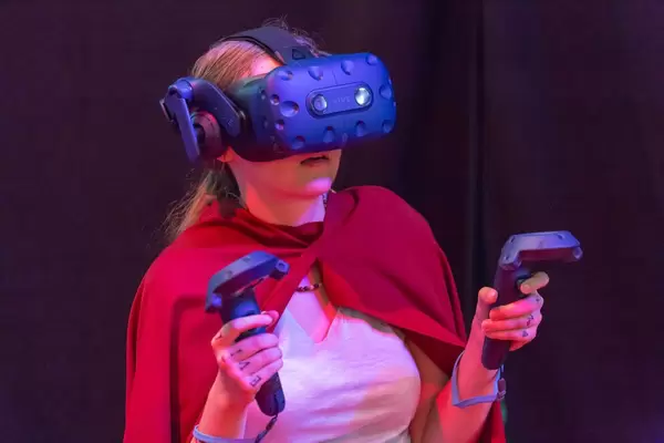 Female visitor with cape gaming with VR headset and controllers