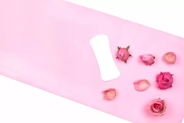 Feminine menstrual pad with pink rose petals on a colored background