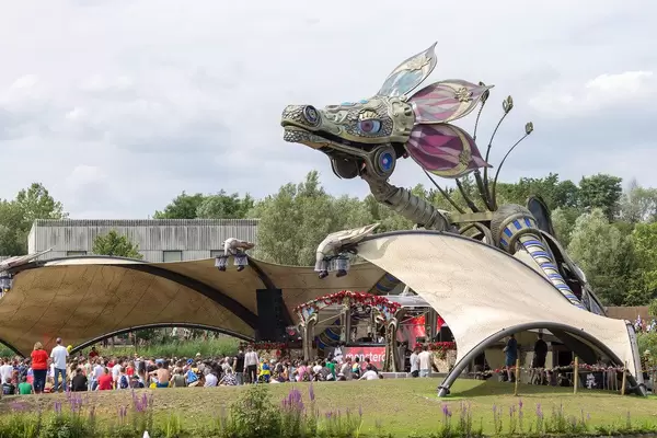 Festivalbesucher von Tomorrowland chillen beim Rose Garden Stage mit einem riesigen metallischen Drachen über ihnen