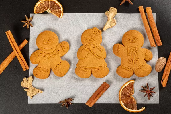 Festive gingerbread men on parchment paper with anise, dried orange, cinnamon and ginger