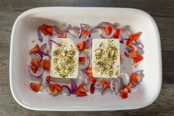 Feta cheese with spices, tomatoes and red onions on a baking plate