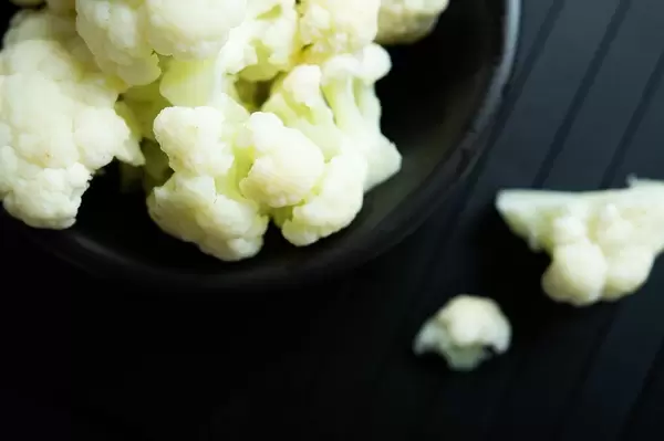 FFlatlay of fresh cauliflower in a bowl on a black wooden table (Flip 2019)