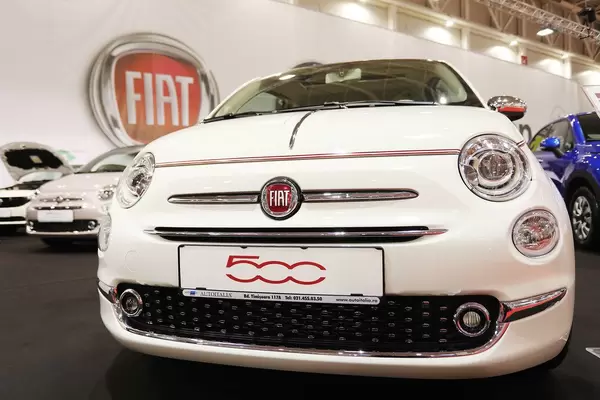 Fiat 500 in Weiß, Aufnahme von vorne mit großem Fiat Logo im Hintergrund