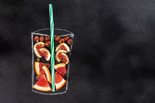 Figs, grapefruit and hazelnuts for blending smoothie in painted glass on black chalkboard. Top view. Healthy eating concept (Flip 2019)