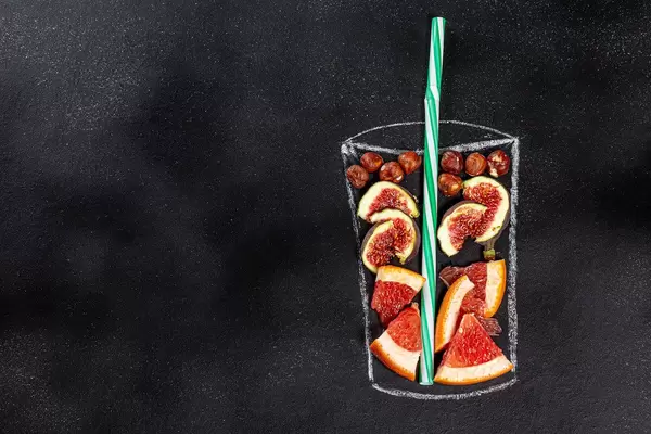 Figs, grapefruit and hazelnuts for blending smoothie in painted glass on black chalkboard. Top view. Healthy eating concept