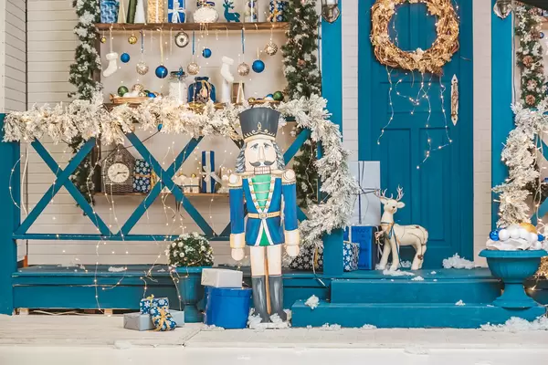 Figurine of a nutcracker near beautifully decorated steps and a door with a wreath