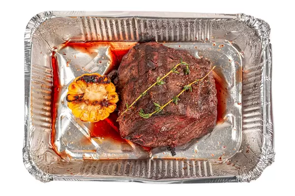 Fillet mignon with thyme sprig and grilled corn in a container, top view