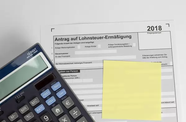 Finanzamt Formular: Leerer Antrag auf Lohnsteuerermäßigung unter gelbem Notizzettel und elektronischen Taschenrechner - Draufsicht