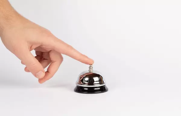 Finger drückt auf alte Hotelklingel vor weißem Hintergrund