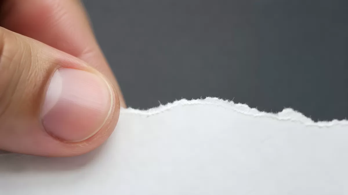 Finger hält zerrissenes weißes Papier in Nahaufnahme