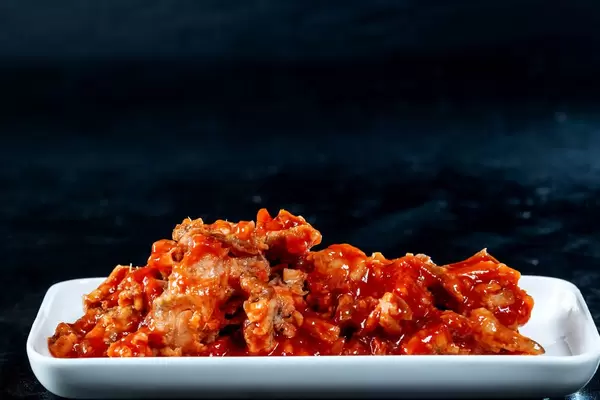 Fischeintopf an Tomatensoße auf weißer Platte vor dunklem Hintergrund