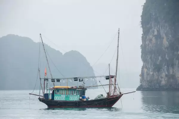 Fischerboot aus Holz auf See von hohen Felswänden umgeben