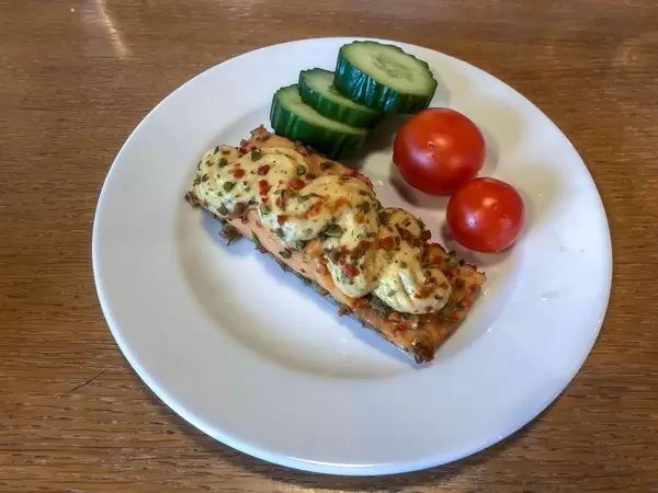 Fischfilet mit Kräuter-Topping, Tomaten und Gurken auf weißem Teller auf einem Holztisch im Pentahotel Berlin, Köpenick