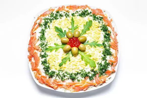 Fish and vegetable salad decorated with fresh herbs, olives and caviar. Top view (Flip 2020)