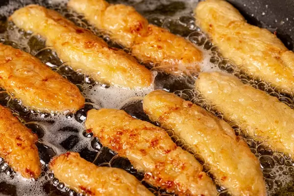 Fish sticks in batter in a frying pan with boiling oil, close-up