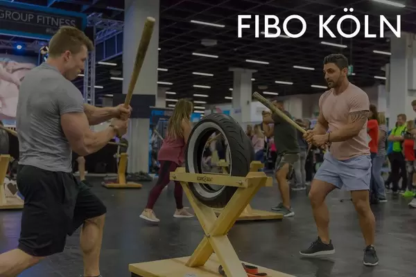 Fitnessmessebesucher beim Krafttraining am funktionalen Allzweck Fitnessgerät Scape Goat, neben dem Bildtitel "Fibo Köln"