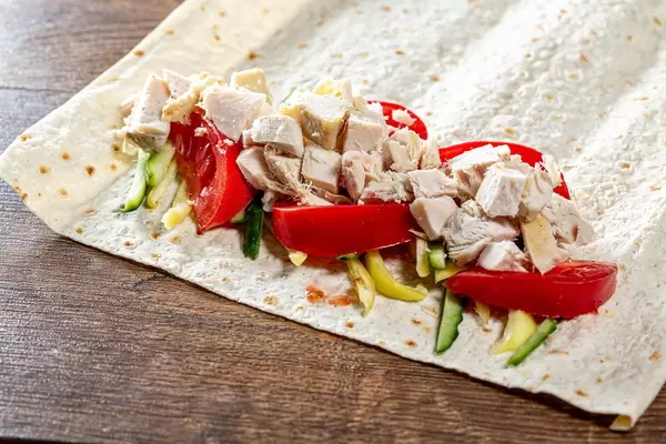 Fladenbrot an einer Seite belegt mit Gemüse und Hähnchen bereit zum einrollen
