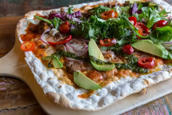 Flame Bread with vegan Chili-Härkis made of horse beans, avocado, chipotle tomato sauce, green salad and tomatoes on a wooden cutting board