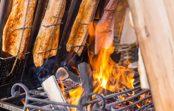 Flame Salmon hanging over Fire coming from Wood in a Barbecue Grill