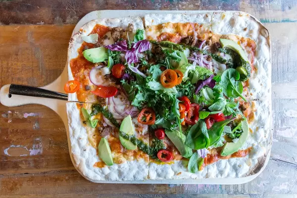 Flammkuchen mit Avocado, Tomatensoße, Salat, Chimichurri, Zwiebeln & veganer Fleischalternative Chili-Härkis, hergestellt aus Ackerbohnen
