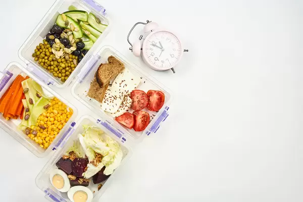 Flat lay arrangement of lunchboxes with organic meal and alarm clock showing lunchtime