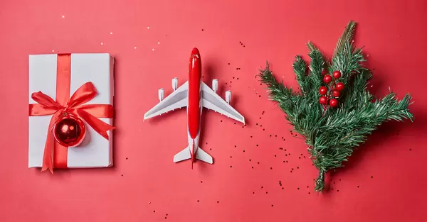 Flat lay composition with toy airplane, gift box and christmas tree on red background