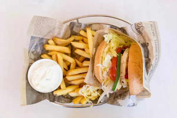 Flat-lay of the Veggie Burger from Bus Burger, packed in old newspaper, with pickles, goat cheese, tomatoes and fries, with a white background