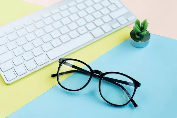 Flat lay with glasses, keyboard and cactus candle on colorful background.