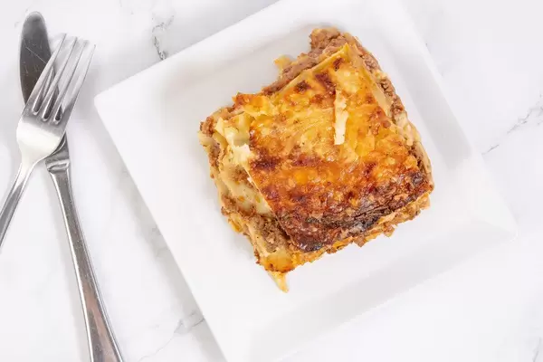 Flatlay einer gebackenen Lasagne auf einem weißen Teller neben Besteck