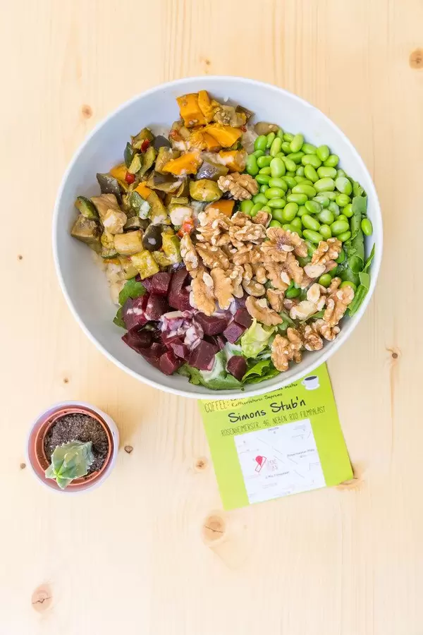 Flatlay of a vegan bowl with various vegetables and a small plant on the wooden table of Simons Stub'n restaurant in Munich