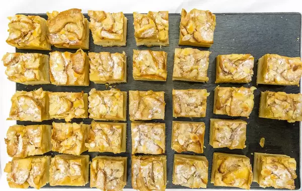 Flatlay of apple-almond cake cut into pieces, on a dark tray