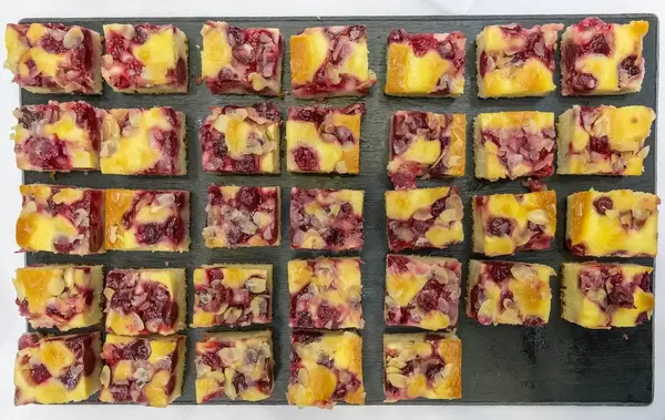 Flatlay of cherry-almond cake cut into pieces, on a black tray