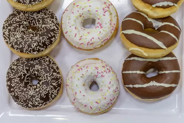 Flatlay of colorful donuts with white and pink glaze, chocolate icing and colorful sprinkles