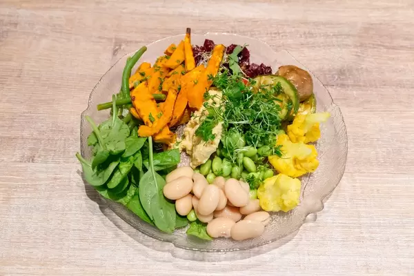 Flatlay of vegan salad with carrots, beetroot, spinach, edamame, cauliflower, mushrooms and other colorful vegetables